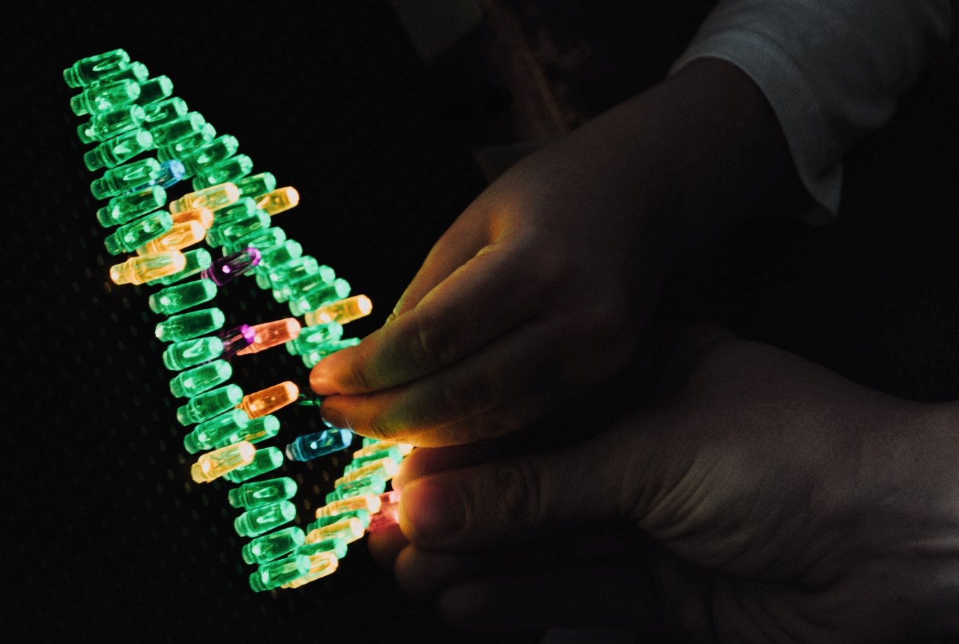 An adult and child hand putting light pegs forming a Christmas tree