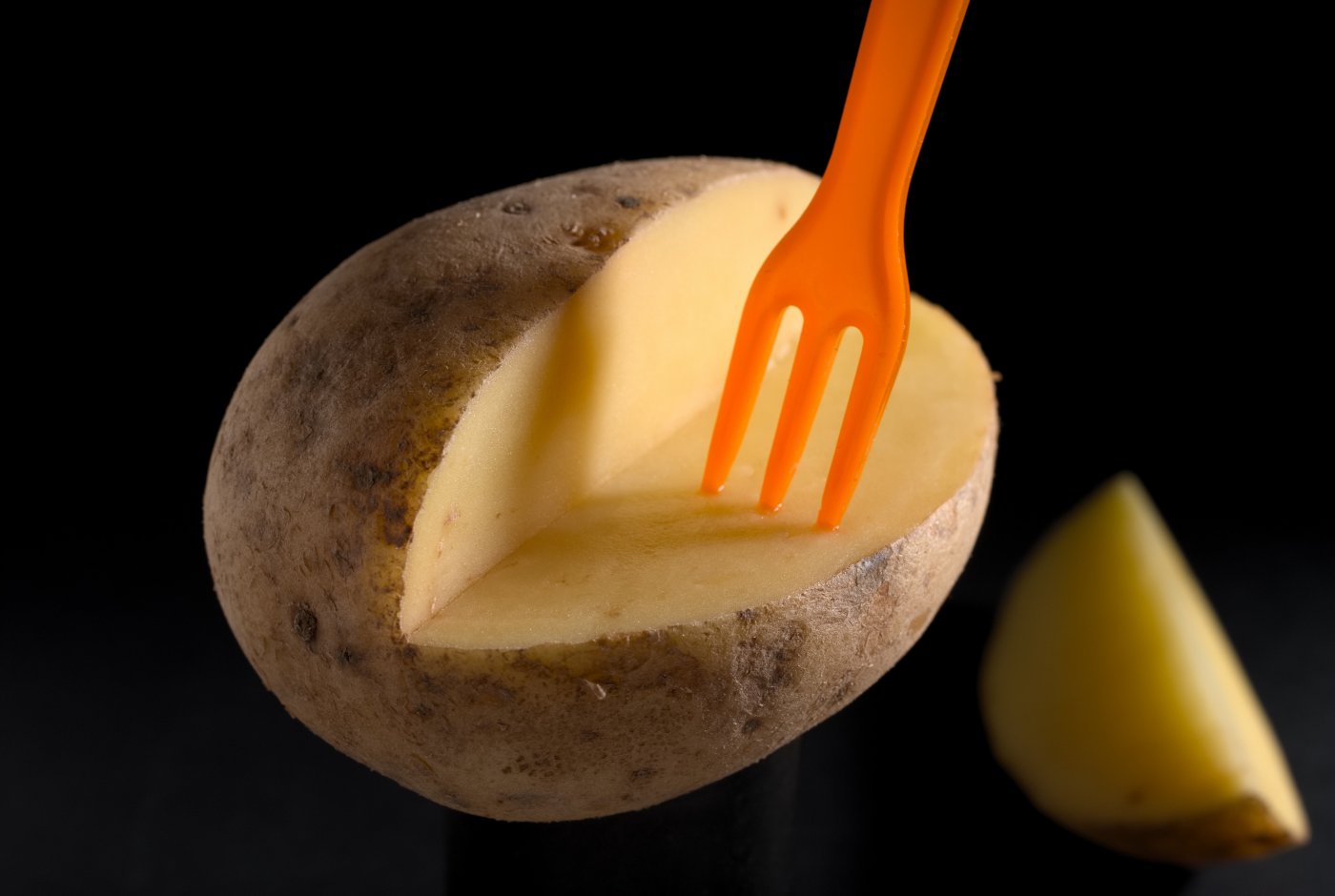 an orange plastic fork sunk in a potato
