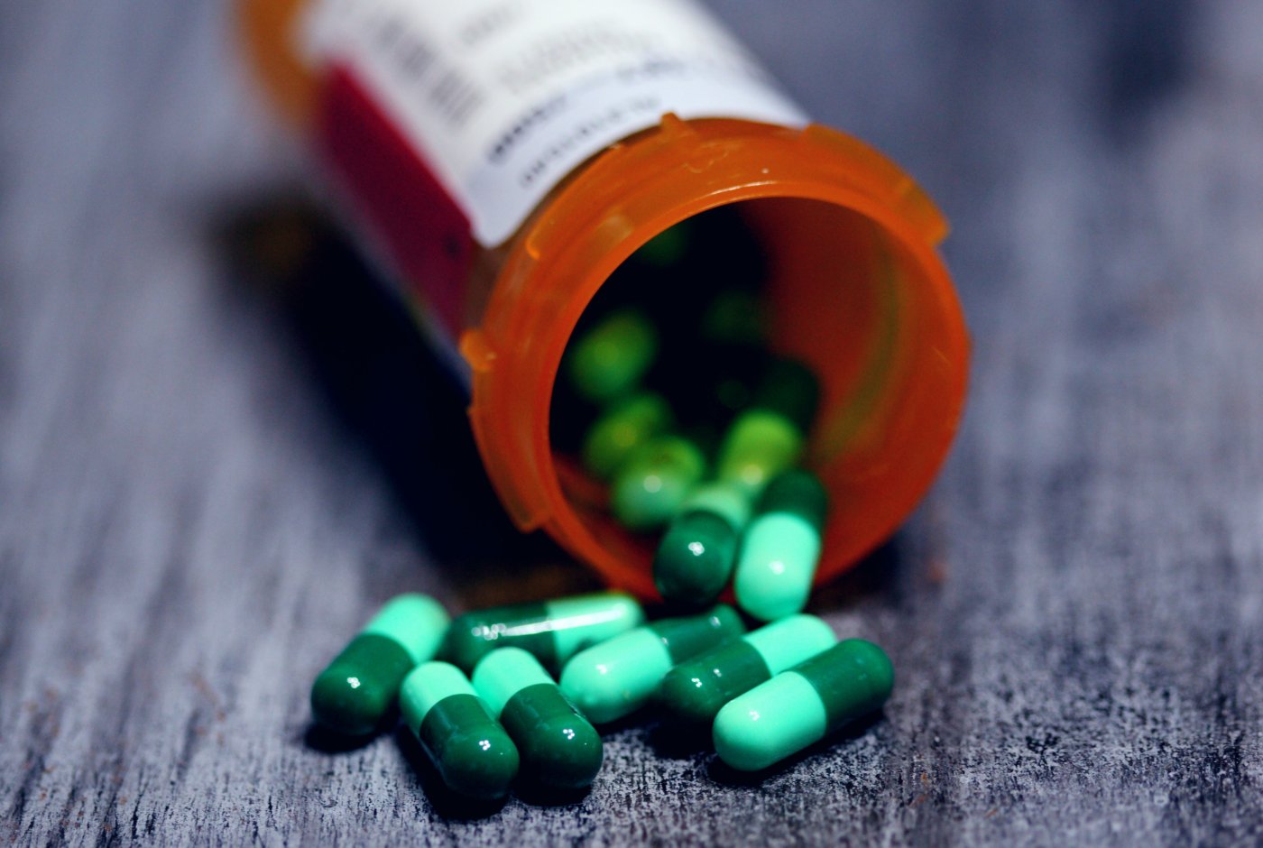 an open pill bottle on its side with green pills falling out
