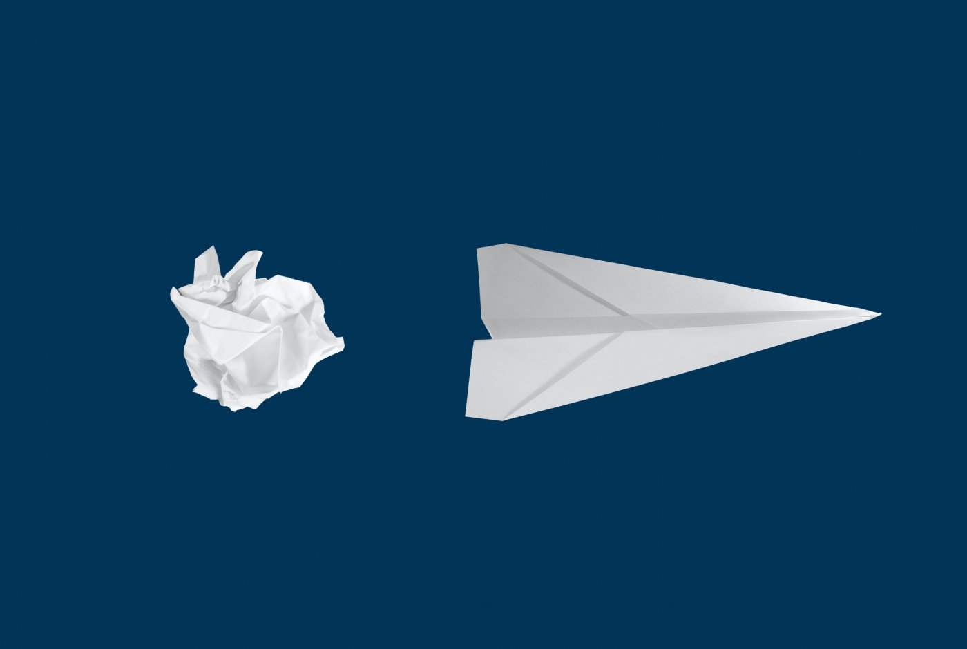 a paper air plane and a crumpled paper on blue background