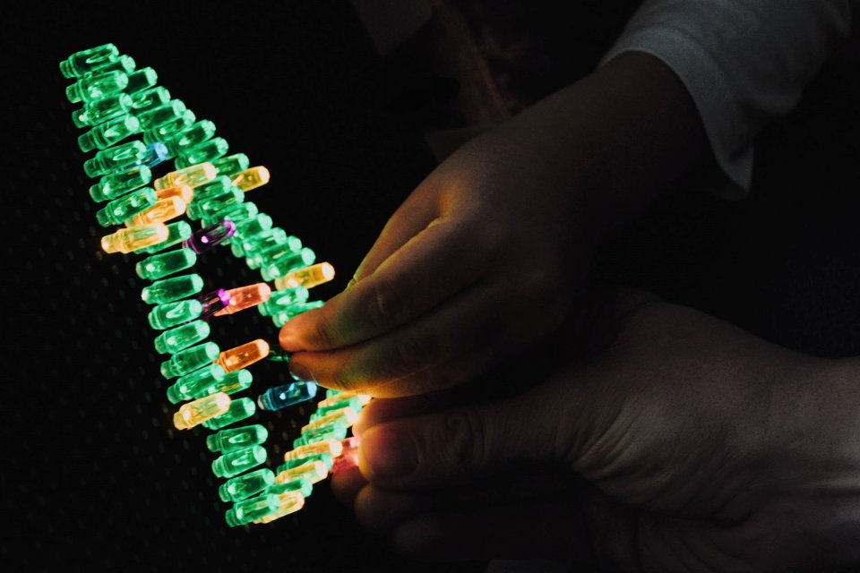 An adult and child hand putting light pegs forming a Christmas tree