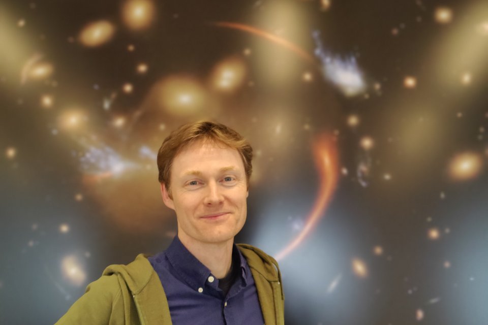 Darach Watson in front of a deep space poster.